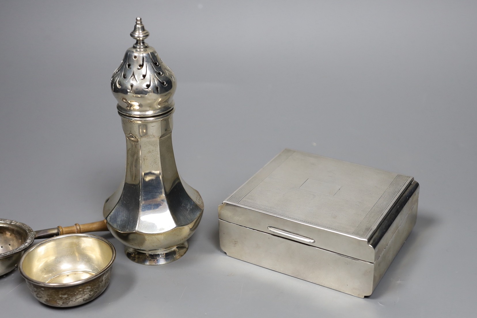 A George V engine turned silver mounted cigarette box, a similar sugar caster and later silver tea strainer and small dish.